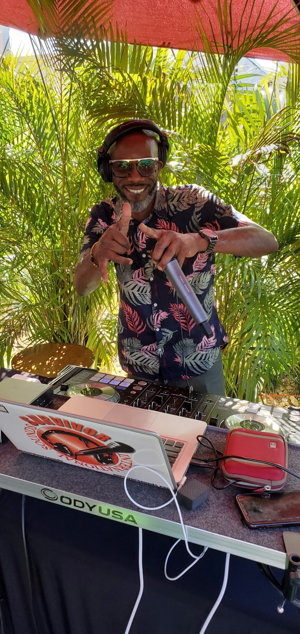 SURVIVORSOUNDS smiling behind the DJ booth at a tropical event